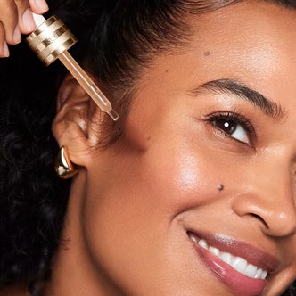 Ulta; a close up of a woman's face and hand holding a dropper applying Estée Lauder Advanced Night Repair Multi-Recovery Complex Serum