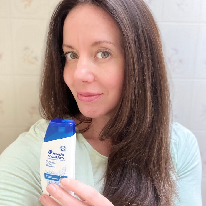 Brittany holding a bottle of Head & Shoulders Classic Clean Shampoo against an off white background