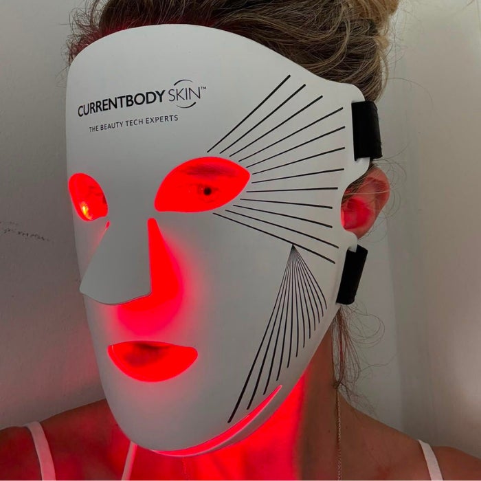 A slightly profile view of a woman's face wearing an LED light therapy mask against a natural background