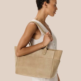 Quince; a woman carrying a Quince Hudson Suede Tote against a neutral background