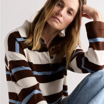 Woman wearing a brown, cream, and light blue striped rugby sweater with a contrasting collar, paired with light-wash jeans for a relaxed preppy look