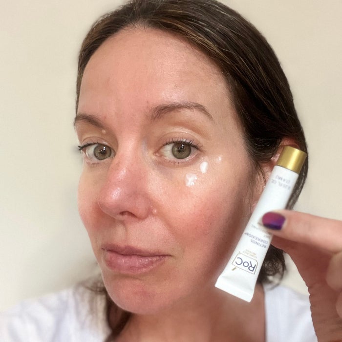 a woman with dots of eye cream under her eye against a beige background
