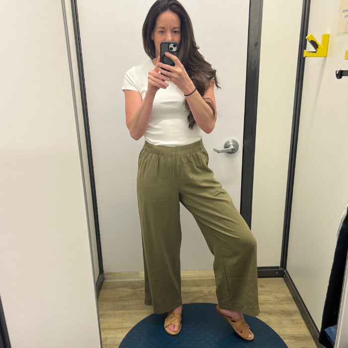 A front view of a woman in khaki linen pant and a white tee shirt against a white dressing room background