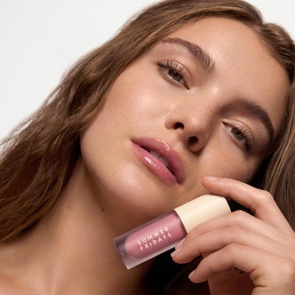 Close-up beauty portrait of a woman holding a Summer Fridays pink lip product against her cheek, wearing a glossy pink lip.