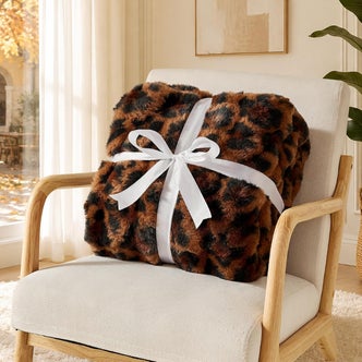 Luxury 1000GSM Faux Rabbit Fur Throw Blanket on a chair with a white bow against a natural background