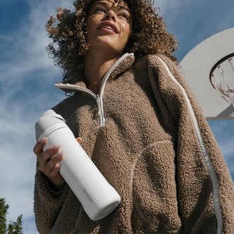A woman holding a Owala water bottle against a natural outdoor background