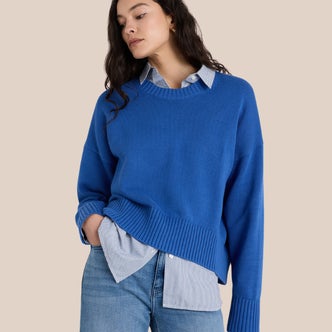 Quince; a woman wearing a Quince 100% Organic Cotton Boyfriend Crew Sweater over a button down shirt against a beige background