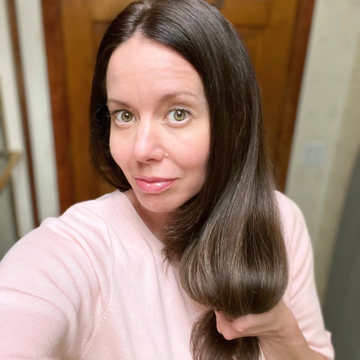 Brittany wearing a pink sweater holding her hair against a natural background