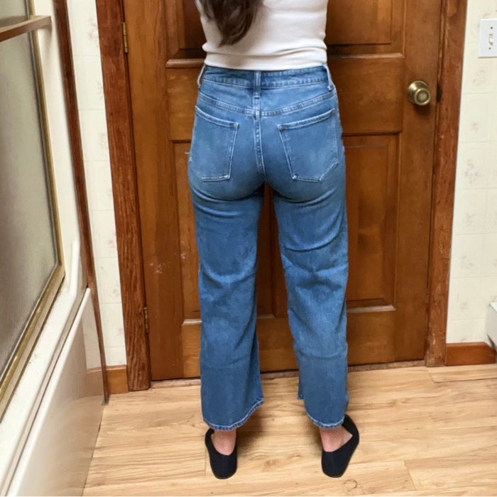 A back view of a woman wearing Bella Stretch Relaxed Straight Jeans against a natural background