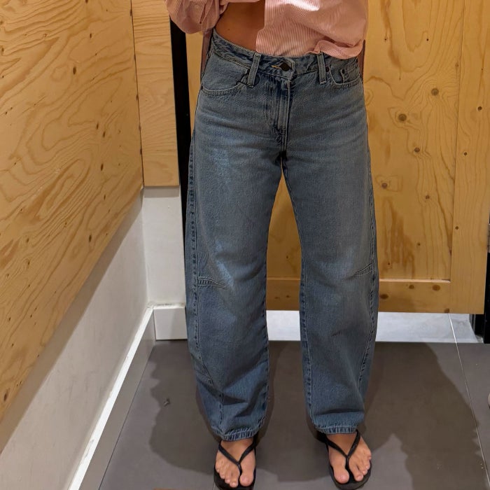 A front view of Anastasia Bilzhause wearing light wash Levi's Cinch Barrel Jeans in a wood paneled dressing room