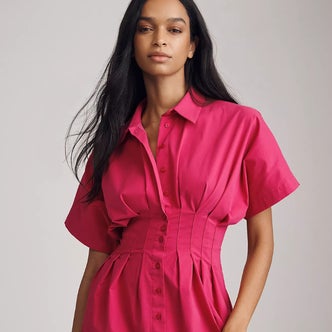 Anthropologie; a woman wearing a pink shirt dress against a neutral background