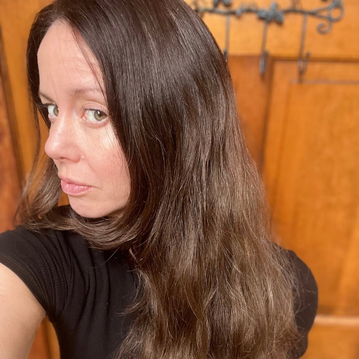 A profile view of a woman's head with slightly frizzy hair against a natural background