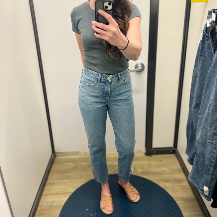 A woman wearing jeans and  a gray shirt against a natural background