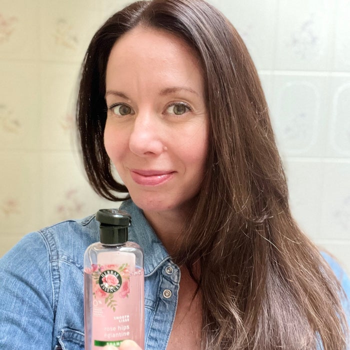Brittany holding a bottle of Herbal Essences Rose Hips Smoothing Shampoo against an off white background