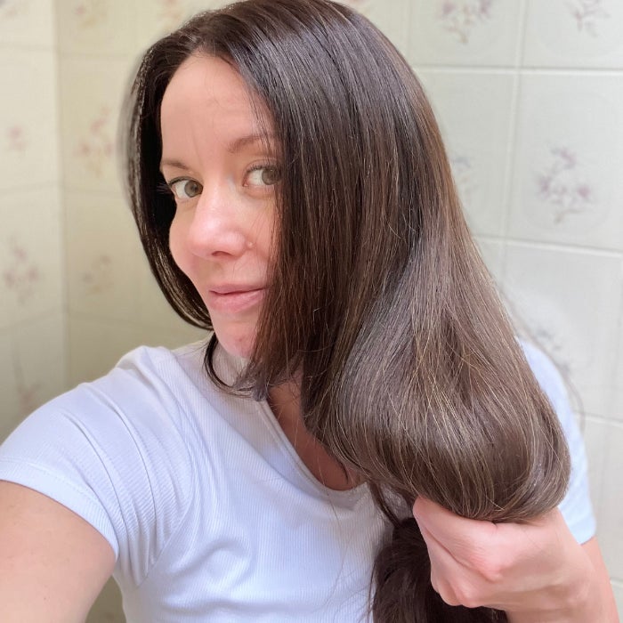 Brittany wearing a white shirt holding her hair against an off white background