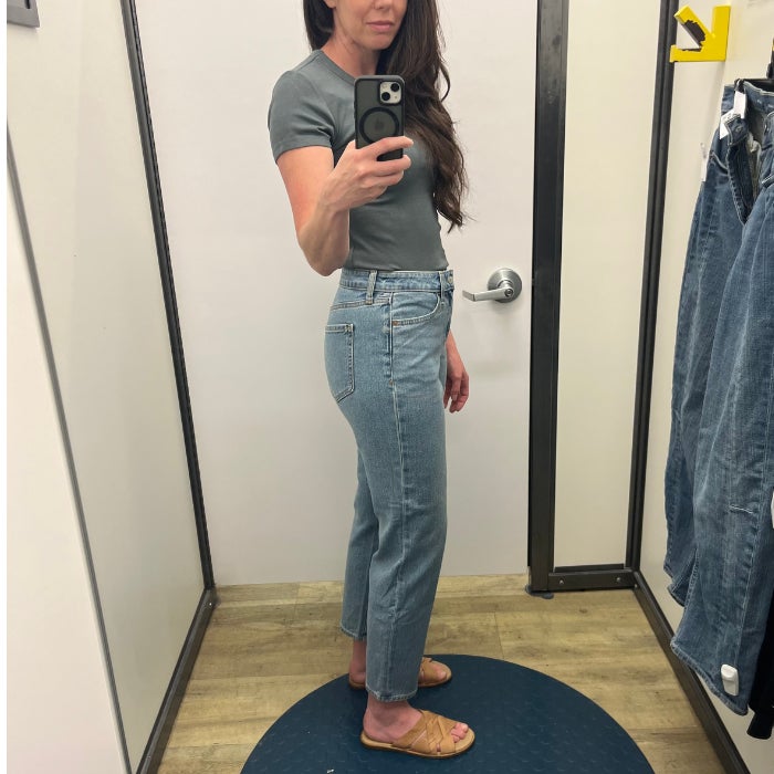 a profile view of a woman wearing jeans and a gray shirt against a natural background