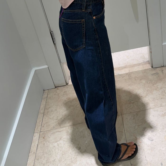 A side profile view of Anastasia Bilzhause wearing dark wash Gap High Rise Barrel Jeans in a white dressing room