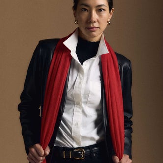 Quince; a woman wearing a white shirt, red scarf, and black jacket against a brown background