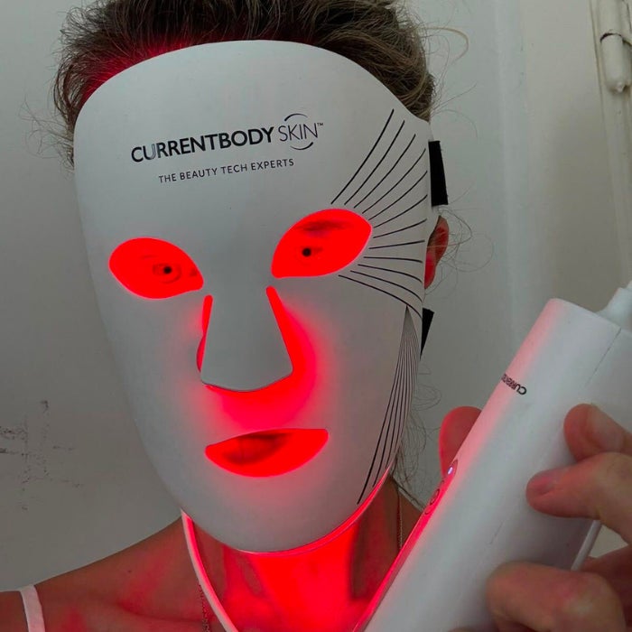 A woman's face wearing an LED light therapy mask against a natural background