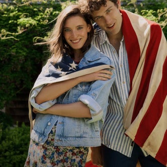 Couple wearing casual summer outfits wrapped in an American flag for a Fourth of July celebration outdoors