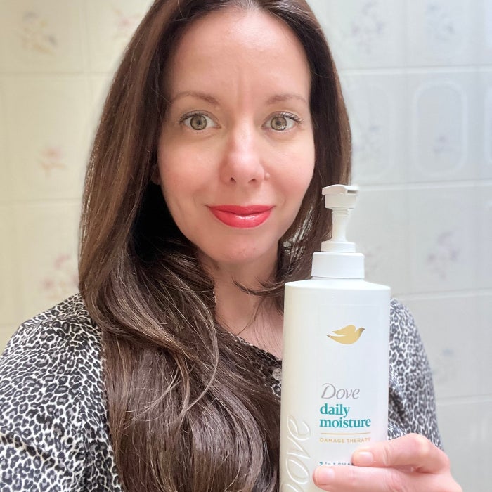 Brittany holding a bottle of Dove Daily Moisture Therapy Shampoo against an off white background